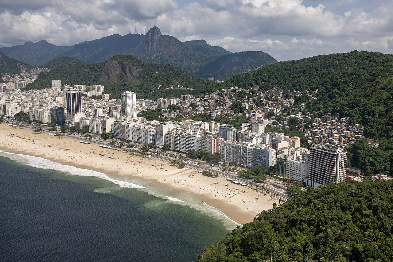 Aerial panorama of Copacabana’s long beach and Rio’s green mountains; this view is illustrative and does not show the accessible beach programme